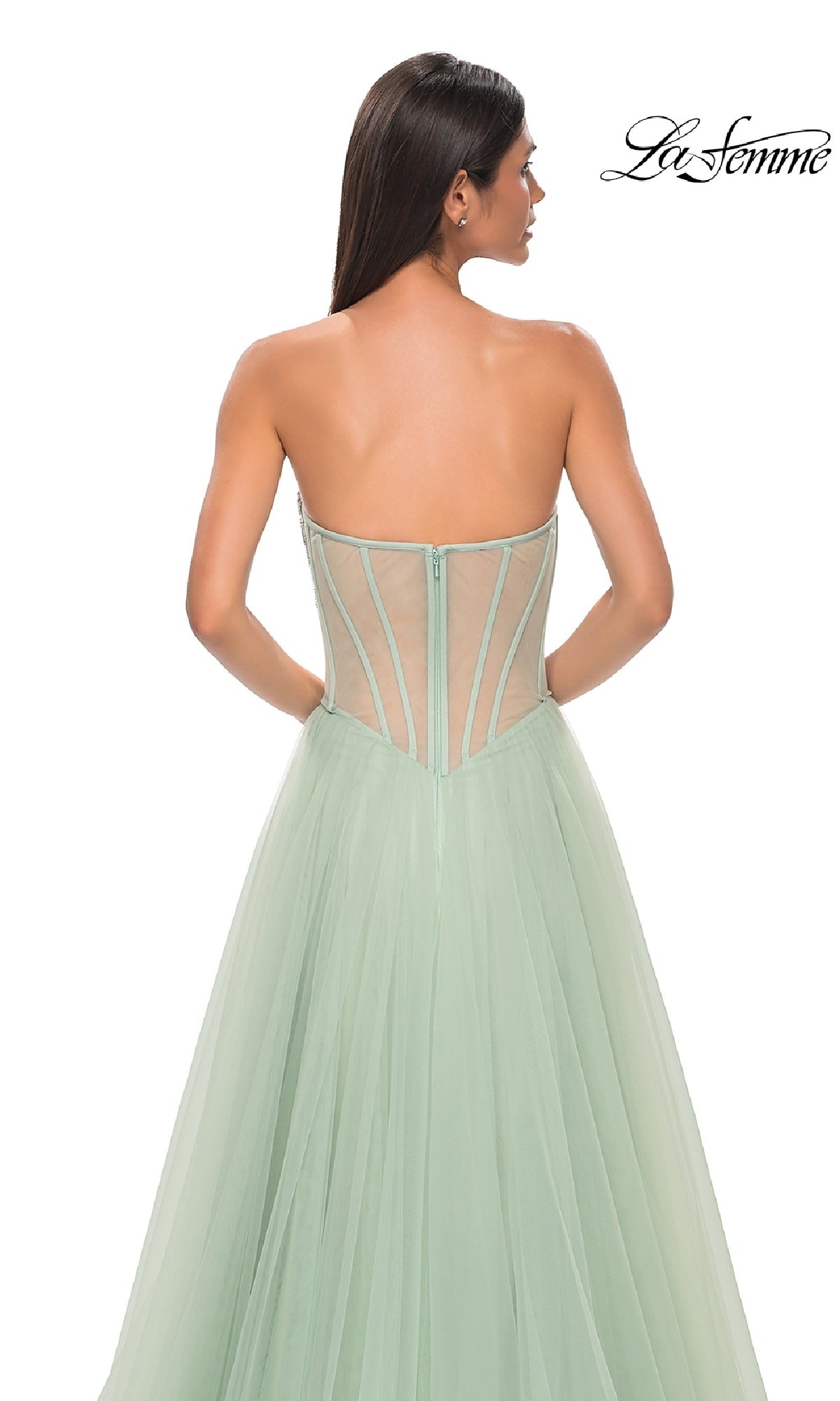 Woman in a strapless mint green La Femme 32811 tulle prom ball gown with visible boning on the bodice, facing away against a white background.